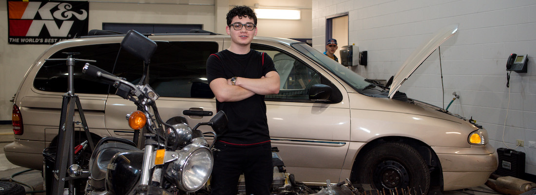 Student in automotive class posing next to a motorcycle and van