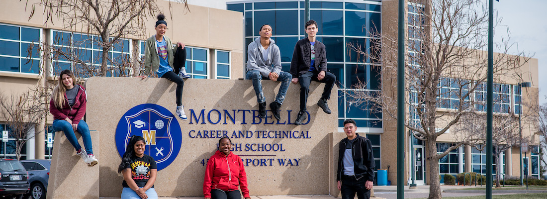 Students in front of school sitting around the sign